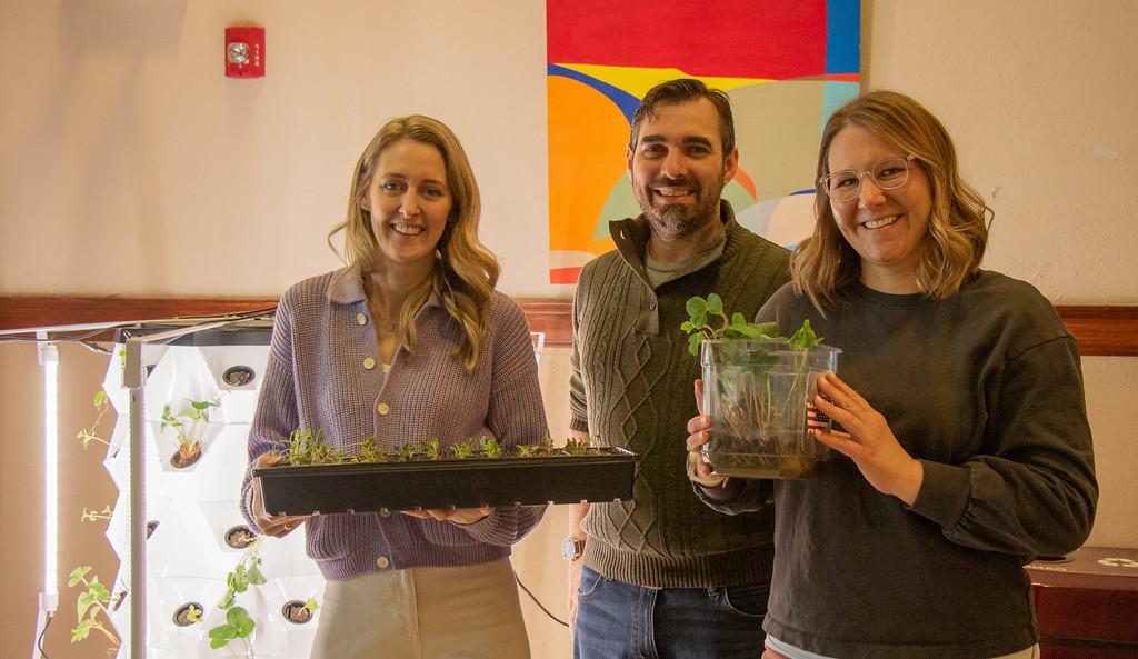 Three adults posing by an indoor plant tower